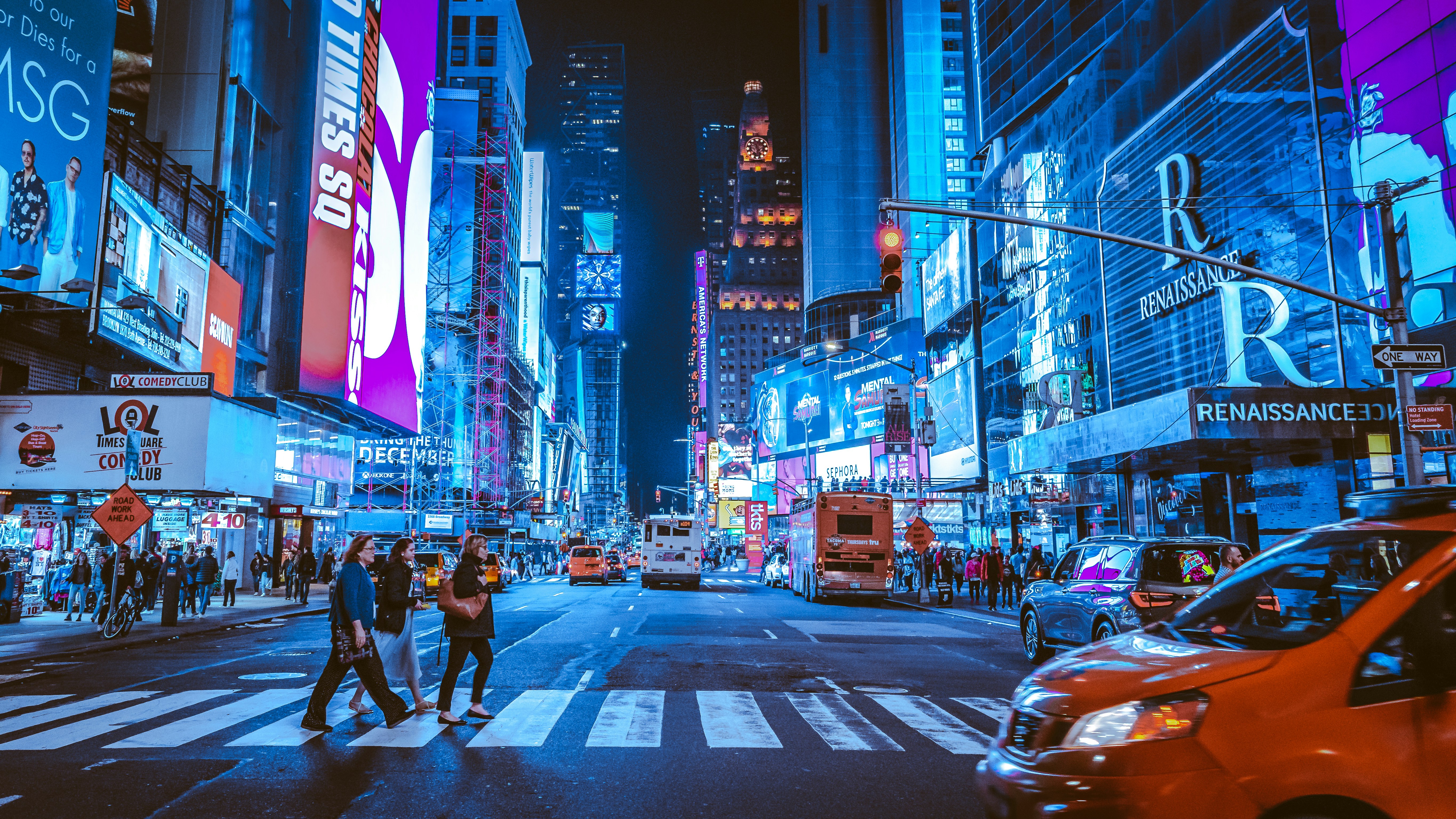 Bustling Times Square at night, with bright neon signs, billboards, pedestrians crossing street, and traffic.